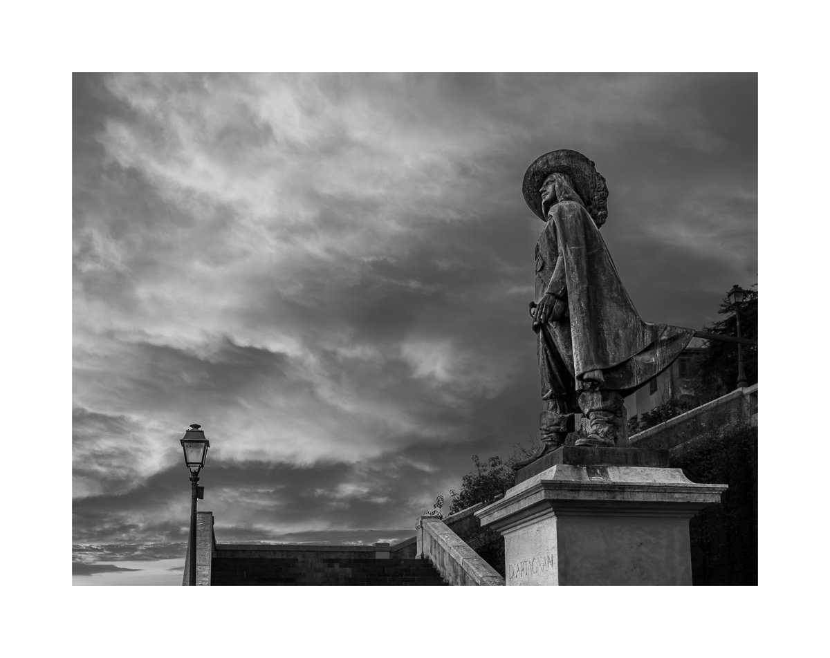 Patrimoine d'Auch : statue d'Artagnan Statue d'Artagnan sous un ciel nuageux, dramatique, à Auch (Gers), photographie noir et blanc